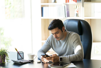 Young man using mobile phone while sitting on table