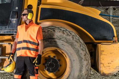 Man standing on land by construction vehicle