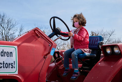 Girl in a mask pretending to drive a tractor at the county fair exhibit