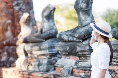 Woman wearing mask and hat looking at ancient temple