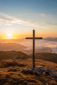 Cross on wooden post against sky during sunset