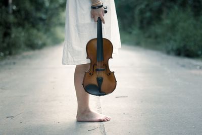 Low section of woman with violin standing on road