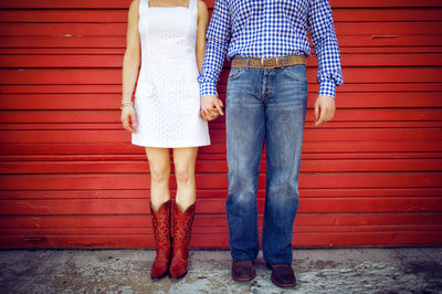 Low section of friends holding hands while standing against closed shutter