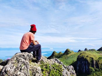 Side view of man sitting on rock against sky