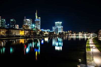 Illuminated buildings by river against sky in city at night