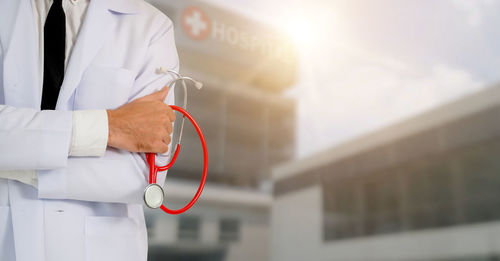 Rear view of doctor with stethoscope standing by hospital outdoors