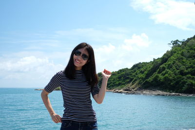 Portrait of young woman wearing sunglasses while standing against sea