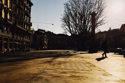 Silhouette bare trees by street against clear sky