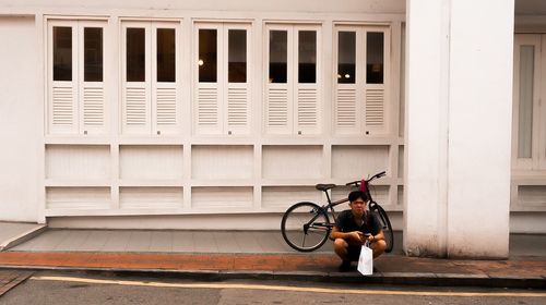 Man sitting on bicycle against building in city