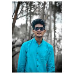 Portrait of young man wearing sunglasses standing against trees