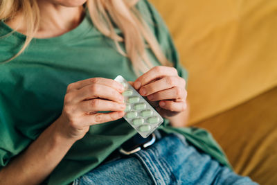 An unrecognizable woman takes one pill out of a pack of pills.