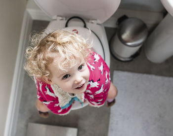 Portrait of happy girl sitting on toilet in bathroom