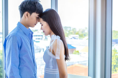 Side view of young woman standing against window