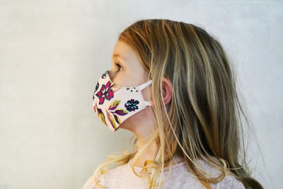 Close-up of cute girl wearing mask standing at home