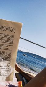 Text on book by sea against clear blue sky