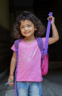 Portrait of cute smiling girl with backpack standing against black background