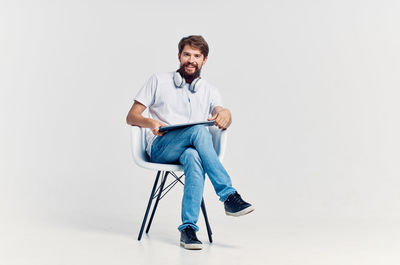 Portrait of young man sitting on chair against white background