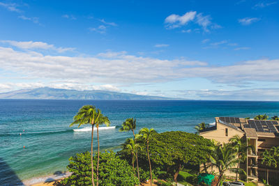 View from high angle of molokai island in distance with palm tress and ocean against sky and clouds