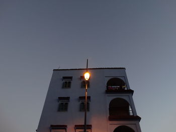 Low angle view of illuminated street light by building against sky at dusk