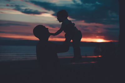 Side view of silhouette father playing with son at beach against sky during sunset