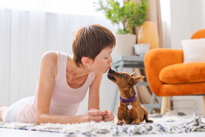 Beautiful adult woman practicing yoga pose with pygmy pinscher dog enjoying