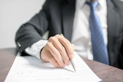 Midsection of businessman signing contract paper at desk in office