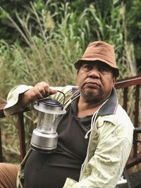 Senior man holding lighting equipment while sitting by railing against plants