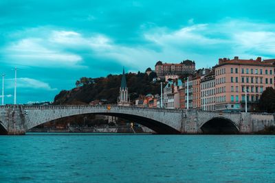 Bridge over river by buildings against blue sky