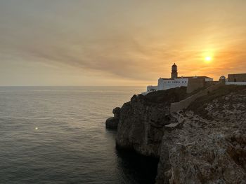 Lighthouse by sea against sky during sunset