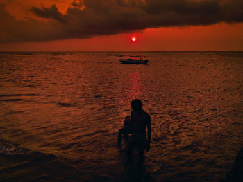 Rear view of man walking at beach against sky during sunset