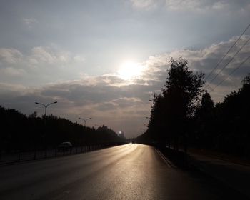 Empty road amidst trees against cloudy sky