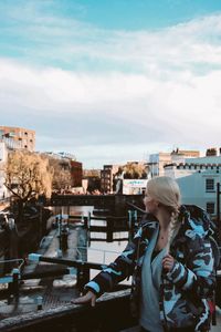 Young woman wearing warm clothing looking at cityscape while standing on building terrace