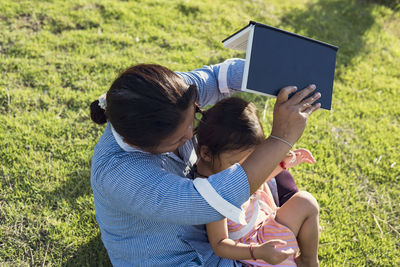 Rear view of woman using digital tablet while sitting on field