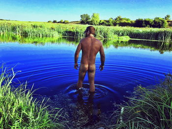 Rear view of shirtless man standing in lake