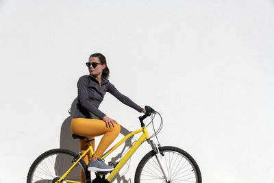 Woman riding a bike looking over her shoulder, white wall background with copyspace.
