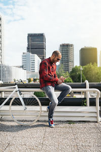 Full length of man with bicycle on city against sky