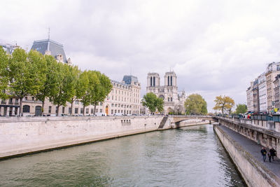 Bridge over river by buildings in city against sky