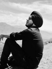 Side view of man looking away while sitting on land against sky