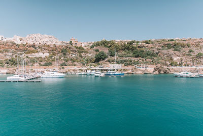 Sailboats in sea by buildings against clear blue sky