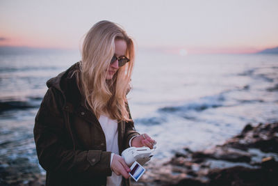 Close-up of young woman standing on beach against sky during sunset