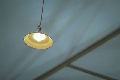 Low angle view of illuminated light bulb hanging from ceiling