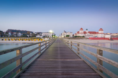 Footbridge over river amidst buildings against clear sky