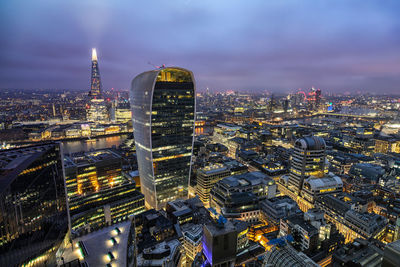 Aerial view of illuminated cityscape against cloudy sky at dusk