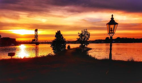 Silhouette trees by lake against sky during sunset