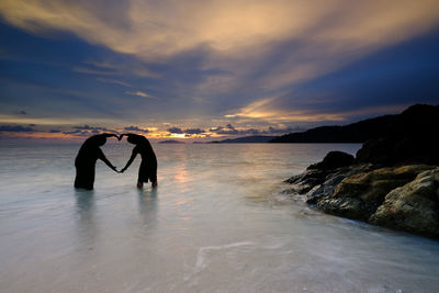 Silhouette men in sea against sky during sunset