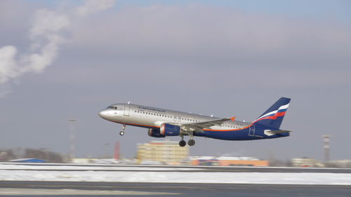 Airplane flying over airport runway against sky