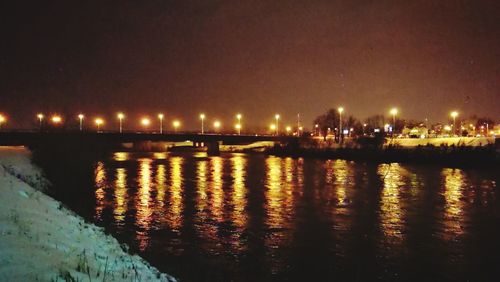 Illuminated city by river against sky at night