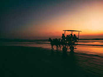 Silhouette people by sea against sky during sunset