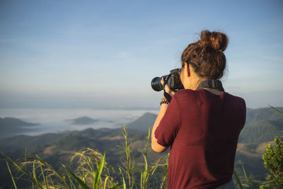 Rear view of woman photographing on field against sky