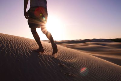 Low section of man walking at desert during sunset
